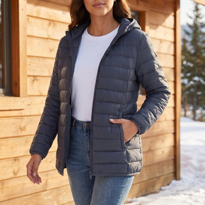 Frau in der grauen Steppjacke vor einer Holzhütte im Schnee