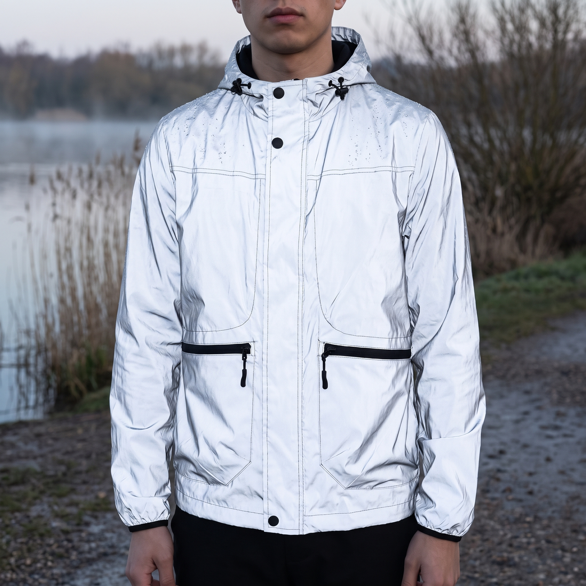Reflektierende Jacke Herren in Silber am nebligen Seeufer in der Dämmerung getragen