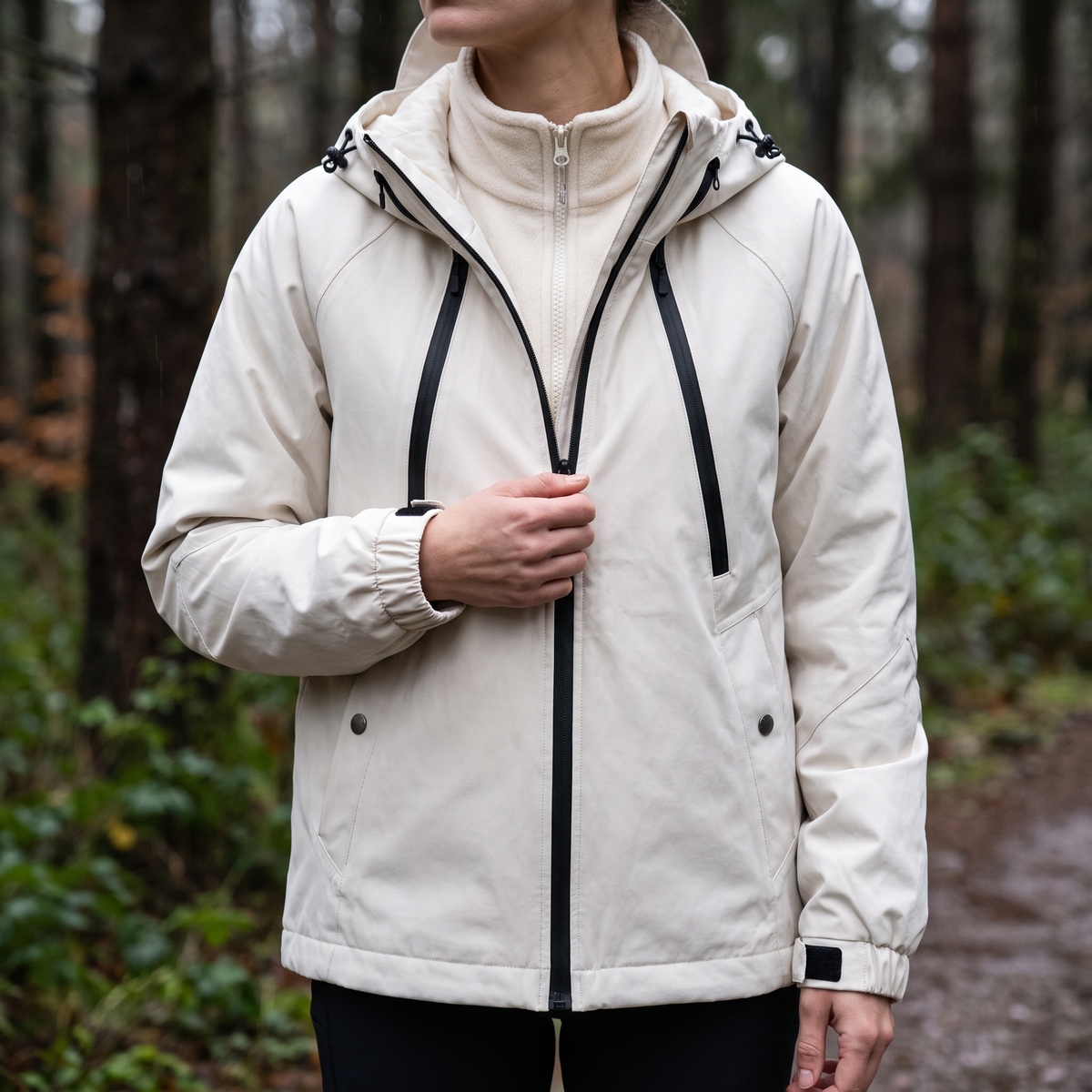 Frau in der weißen 3-in-1 Wanderjacke im Wald, Fleecefutter unter der geöffneten Außenjacke sichtbar