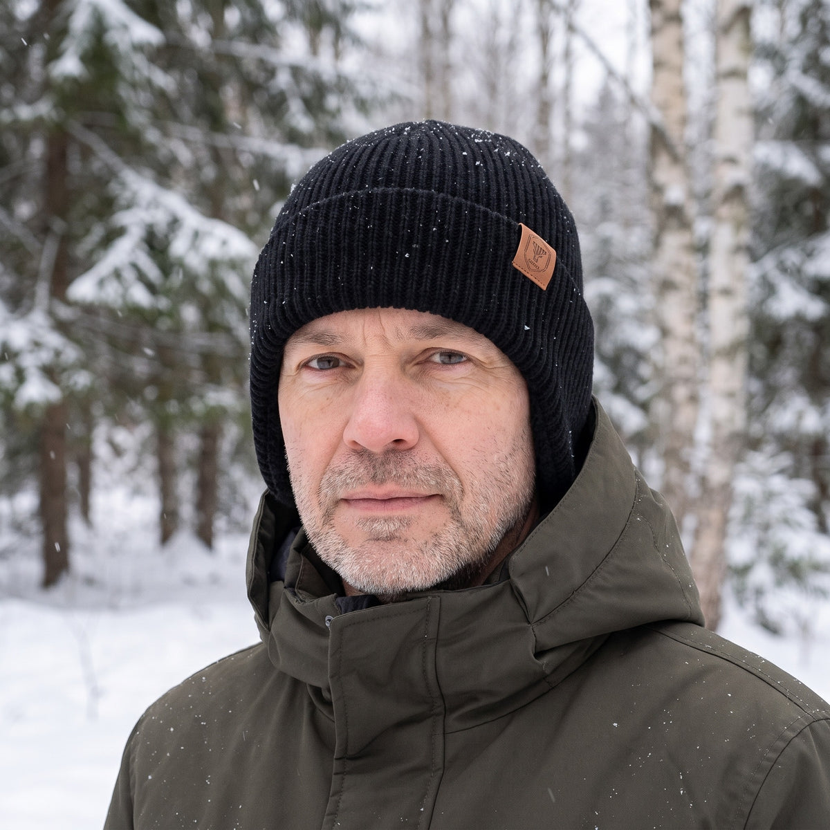 Mütze mit Ohrenklappen in Schwarz getragen im verschneiten Wald