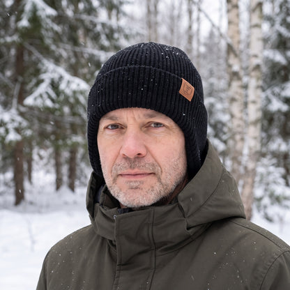 Mütze mit Ohrenklappen in Schwarz getragen im verschneiten Wald